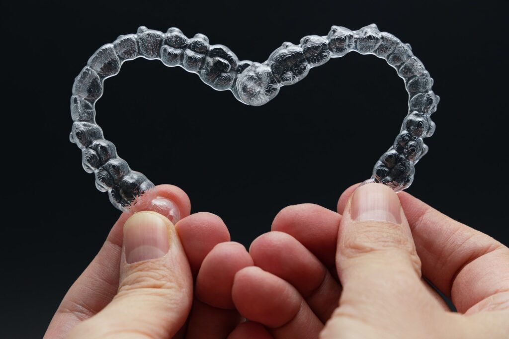 Hands holding dental aligners in heart shape on black background