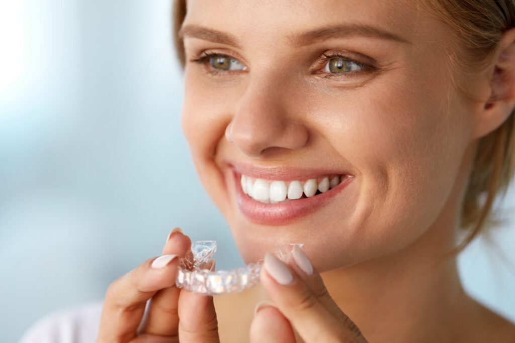 Patient smiling holding Invisalign clear aligners